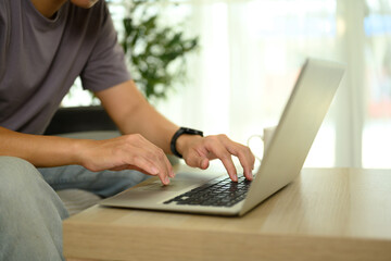 Close up of man working on laptop at home, typing on keyboard at wooden table