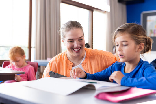 In school, female teacher helping boy with reading assignment in classroom