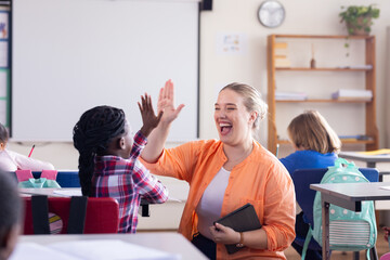 High-fiving african american girl in classroom, female teacher celebrating achievement in school