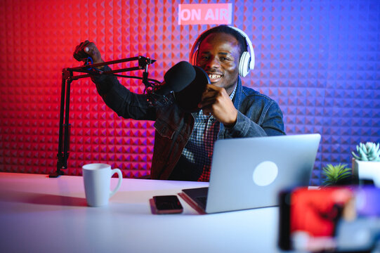 african american vlogger using smartphone to film podcast in studio. blogger with mobile phone, microphone and headphones filming video