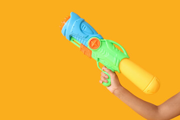 Hand of woman with water gun on yellow background