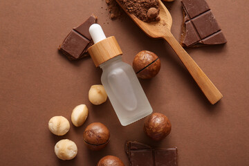 Macadamia nuts, chocolate, cocoa, wooden scoop and bottle of cosmetic product on brown background, closeup