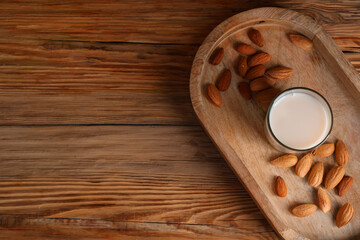 Glass of fresh almond milk and tray with nuts on wooden background