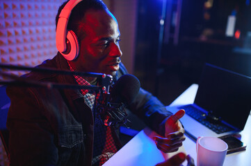Young african american man recording or streaming podcast using microphone at his small broadcast...