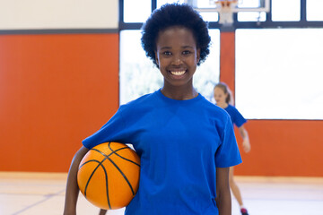 In school gym, african american girl holding basketball, smiling and ready to play
