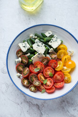 Salad with cherry tomatoes, green beans and blue cheese, vertical shot on a white stone background, elevated view, middle close-up