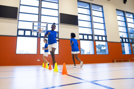 Fototapeta Running through cones, diverse girls participating in physical education class at school gym