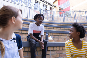 In school, three diverse kids sitting on steps, talking and enjoying break time