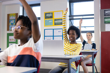 In school, diverse students raising hands in classroom, participating in lesson actively