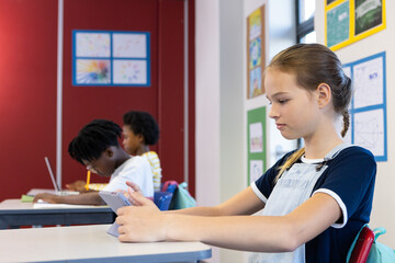 In school, girl using tablet while classmates studying at desks in classroom
