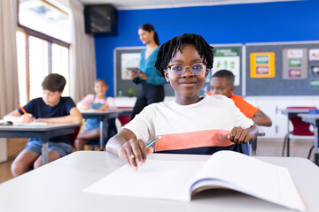 In school, student writing in notebook while classmates studying in classroom