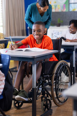 In school, boy in wheelchair writing in notebook, smiling in classroom