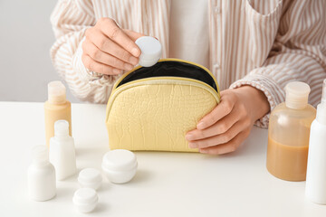 Woman putting travel cosmetic products into bag at light table, closeup