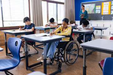 In school, students writing in notebooks at desks in classroom with Indian female teacher