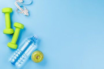 Flat lay of dumbbells, water bottle, and green apple over a bright blue
