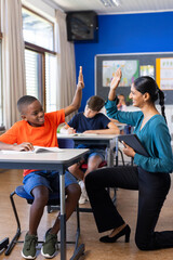 In school, Indian female teacher high-fiving student while holding tablet in classroom
