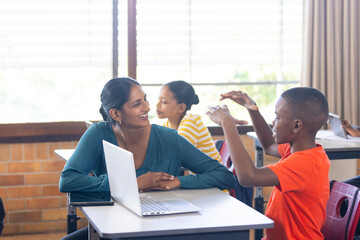 In school, Indian female teacher with laptop engaging with students in classroom discussion