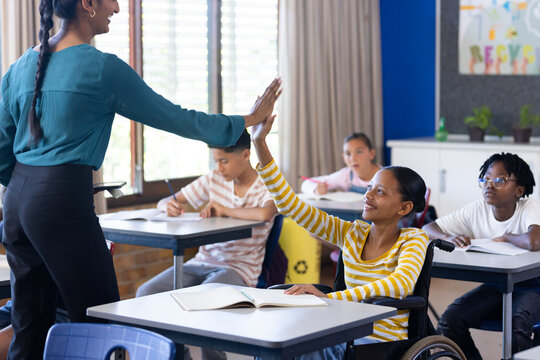 In school, Indian female teacher high-fiving student in wheelchair during classroom activity