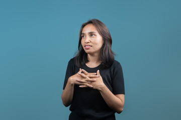 An Indonesian woman smiles subtly with fingers interlocked and eyes slightly looking up, appearing...