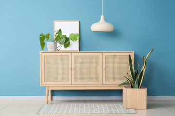 Chest of drawers with houseplants, lamp and frame near blue wall in room