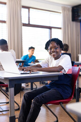 In school, boy using laptop in classroom, smiling and looking at camera