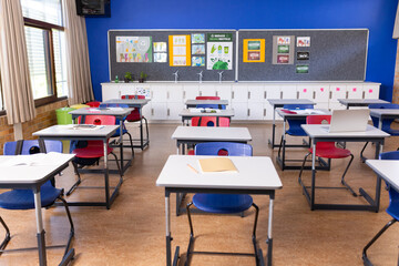 Empty classroom with desks and chairs neatly arranged, ready for students, copy space