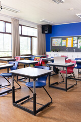 Empty classroom with colorful chairs and desks arranged neatly for students, copy space