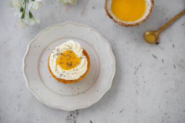 Lemon Poppy Seed Cupcakes with lemon curd and cream cheese topping. Cupcake in form of Fried Egg. Colourful Easter eggs, flowers on a stone background. Spring concept. Easter holiday and festive food.