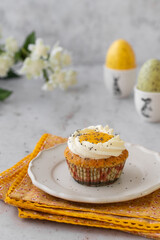 Lemon Poppy Seed Cupcakes with lemon curd and cream cheese topping. Cupcake in form of Fried Egg. Colourful Easter eggs, flowers on a stone background. Spring concept. Easter holiday and festive food.