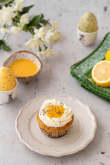 Lemon Poppy Seed Cupcakes with lemon curd and cream cheese topping. Cupcake in form of Fried Egg. Colourful Easter eggs, flowers on a stone background. Spring concept. Easter holiday and festive food.