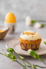 Lemon Poppy Seed Cupcakes with lemon curd and cream cheese topping. Cupcake in form of Fried Egg. Colourful Easter eggs, flowers on a stone background. Spring concept. Easter holiday and festive food.