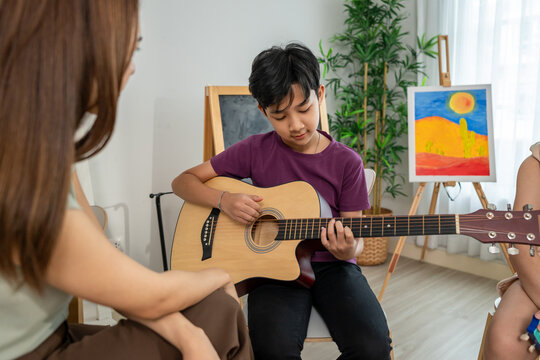 Asian teacher educating students in guitar class at elementary school. 