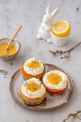 Lemon Poppy Seed Cupcakes with lemon curd and cream cheese topping. Cupcake in form of Fried Egg. Colourful Easter eggs, flowers on a stone background. Spring concept. Easter holiday and festive food.