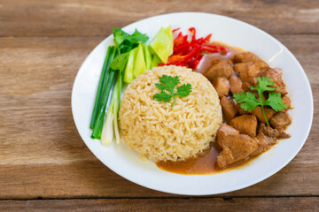Chinese style chicken gravy fragrant with sesame oil and steamed jasmine brown rice with side dishes of scallions, cucumber, cilantro, red chilli in white plate on wooden table.