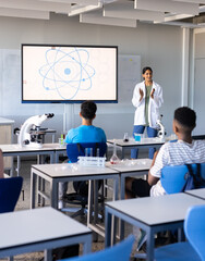 Explaining science concept in school, indian female teacher with students using microscopes