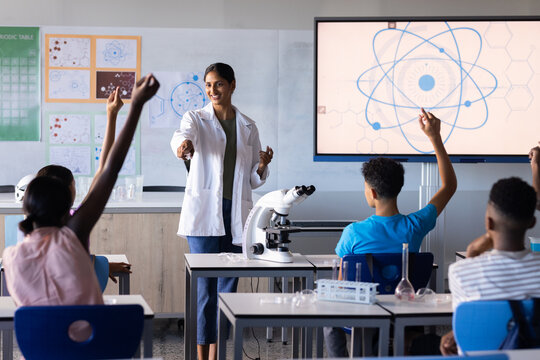 In school, Indian female teacher engaging students in science lesson with microscope and screen