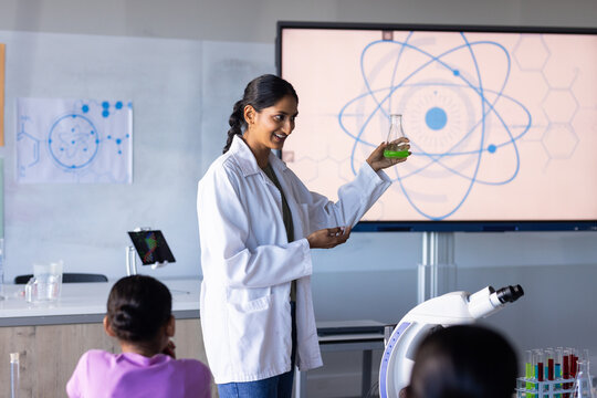 Holding flask and explaining experiment, woman teaching science to students in school
