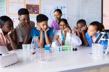 In school, students observing Indian female teacher conducting science experiment with test tubes