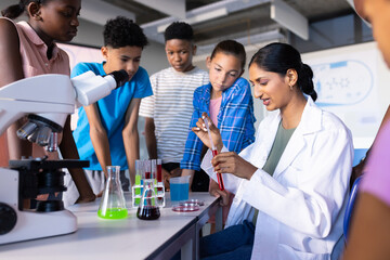 Demonstrating science experiment in school, indian female teacher using microscope and test tubes