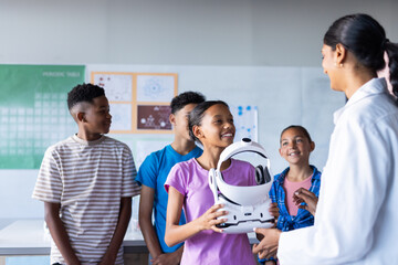 In school, students interacting with Indian female teacher while holding VR headset in classroom © wavebreak3