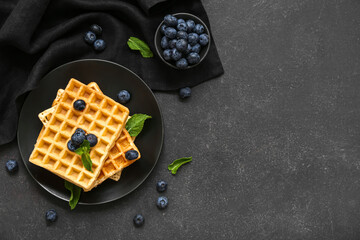 Plate of sweet Belgian waffles with fresh blueberries and mint on black background