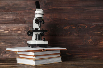 Modern microscope with books on table against wooden background