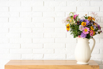 Vase with wild flowers on chest of drawers near white brick wall in room. Closeup