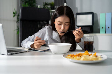 Asian young businesswoman eating noodles while working in the office. 