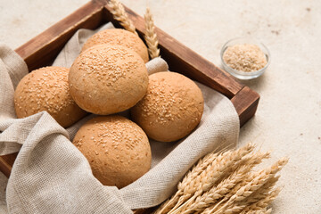 Wooden board of fresh buns with sesame seeds and wheat on white background