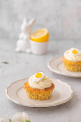 Lemon Poppy Seed Cupcakes with lemon curd and cream cheese topping and Fried Egg candies. Colourful Easter eggs, flowers on a stone background, top view. Easter holiday and festive food.