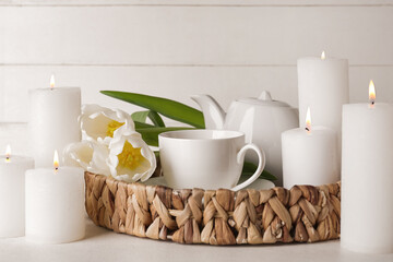 Burning candles with teapot, cup of tea and beautiful tulip flowers on white table