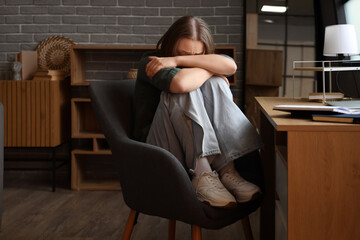 Scared young woman sitting in armchair at home. Domestic violence concept