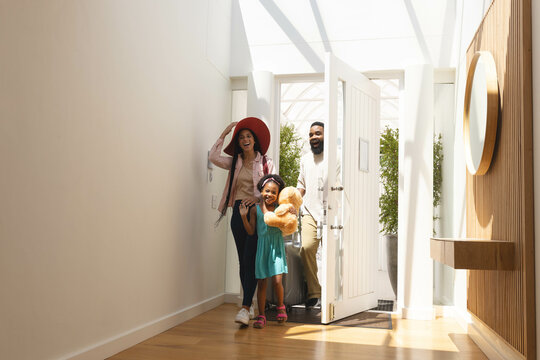 Happy family entering home, smiling and carrying teddy bear in bright hallway, copy space - Powered by Adobe