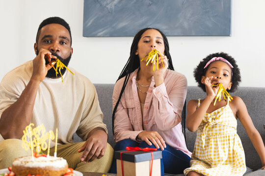 Blowing party horns, Happy family celebrating birthday on couch, looking joyful, at home